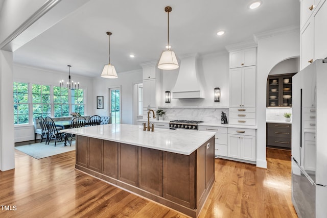 kitchen featuring white fridge, white cabinetry, custom range hood, an island with sink, and light hardwood / wood-style floors