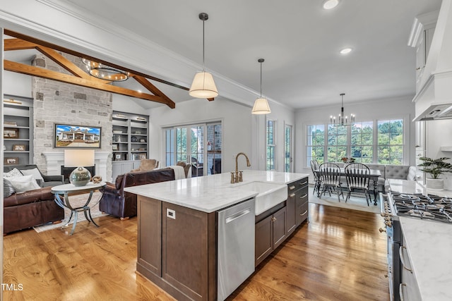 kitchen with a stone fireplace, light hardwood / wood-style floors, stainless steel appliances, sink, and pendant lighting