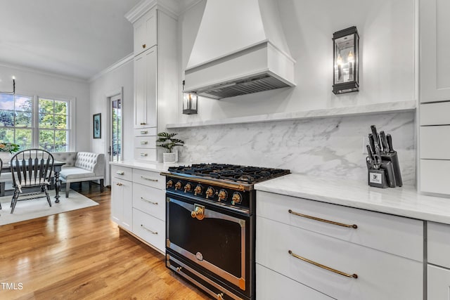 kitchen with light stone counters, high end range, custom range hood, white cabinetry, and light hardwood / wood-style flooring