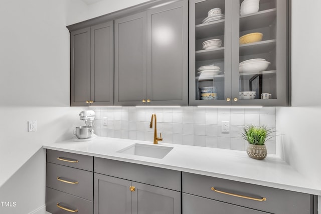 bar featuring gray cabinets, sink, and backsplash