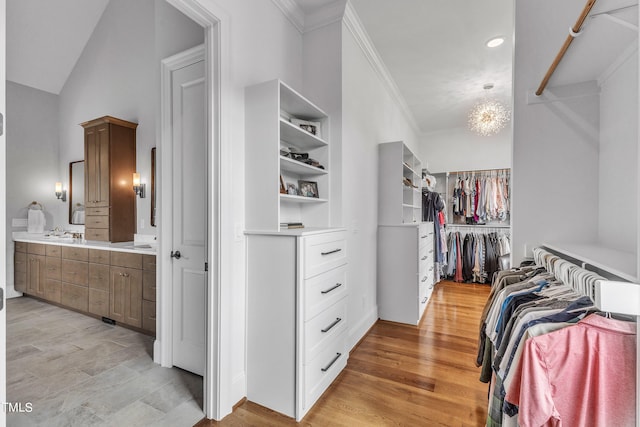 walk in closet with light wood-type flooring, lofted ceiling, and a chandelier