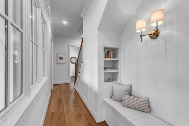 hallway featuring built in shelves, wood-type flooring, and crown molding