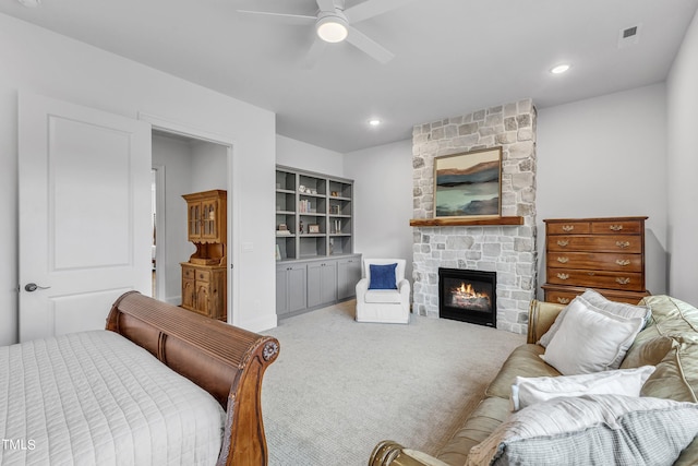 carpeted bedroom with a stone fireplace and ceiling fan