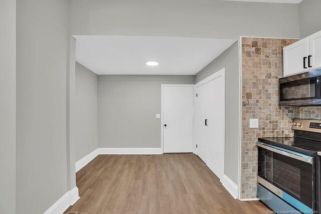 interior space featuring light wood-type flooring, stainless steel electric range, a fireplace, and white cabinets