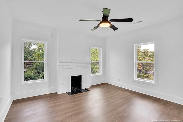 unfurnished living room featuring dark wood-type flooring, ceiling fan, a wealth of natural light, and a fireplace