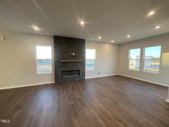 unfurnished living room with dark hardwood / wood-style floors, a wealth of natural light, and a tiled fireplace