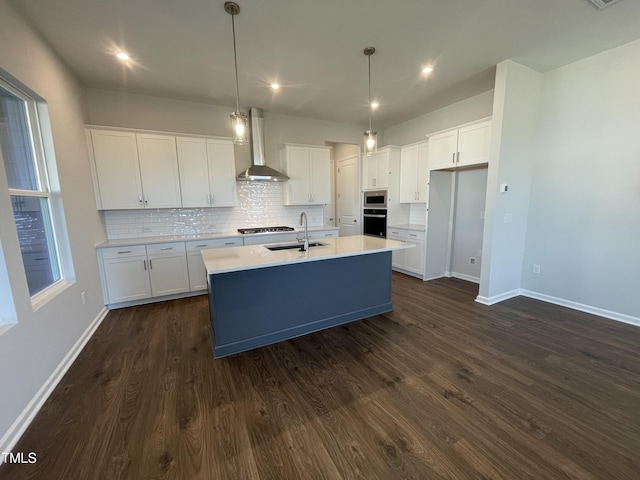 kitchen with white cabinets, wall chimney exhaust hood, sink, and a kitchen island with sink