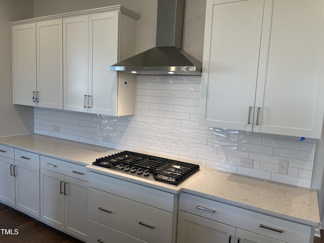 kitchen featuring backsplash, light stone counters, wall chimney exhaust hood, white cabinets, and stainless steel gas stovetop