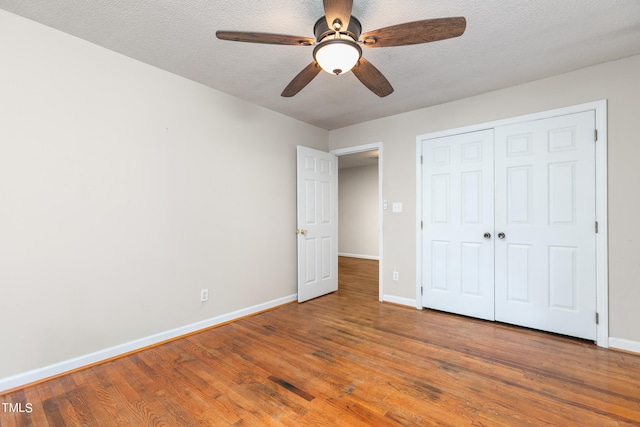 unfurnished bedroom featuring a closet, ceiling fan, wood-type flooring, and a textured ceiling