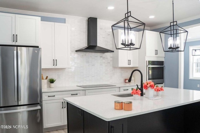 kitchen with wall chimney range hood, white cabinetry, a center island with sink, and stainless steel refrigerator