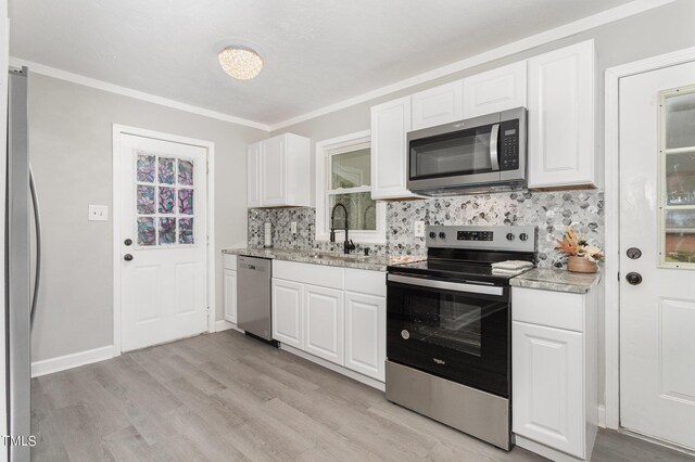 kitchen with white cabinets, appliances with stainless steel finishes, light hardwood / wood-style floors, sink, and ornamental molding