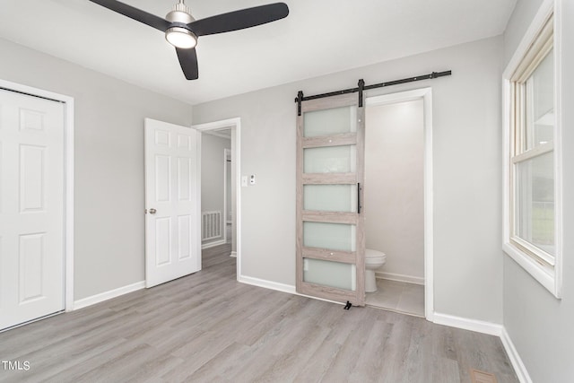 unfurnished bedroom featuring visible vents, connected bathroom, baseboards, a barn door, and wood finished floors