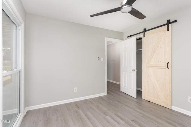 unfurnished bedroom with a barn door, wood finished floors, baseboards, and ceiling fan