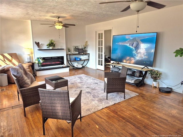 living room with ceiling fan, wood-type flooring, french doors, and a textured ceiling