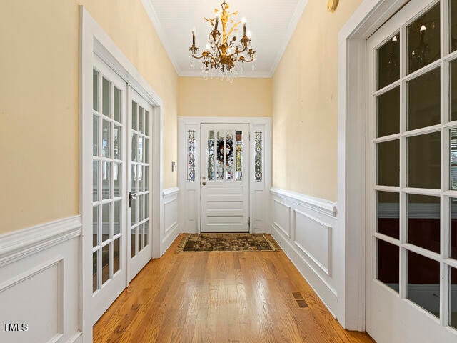 entryway featuring an inviting chandelier, hardwood / wood-style flooring, french doors, and crown molding