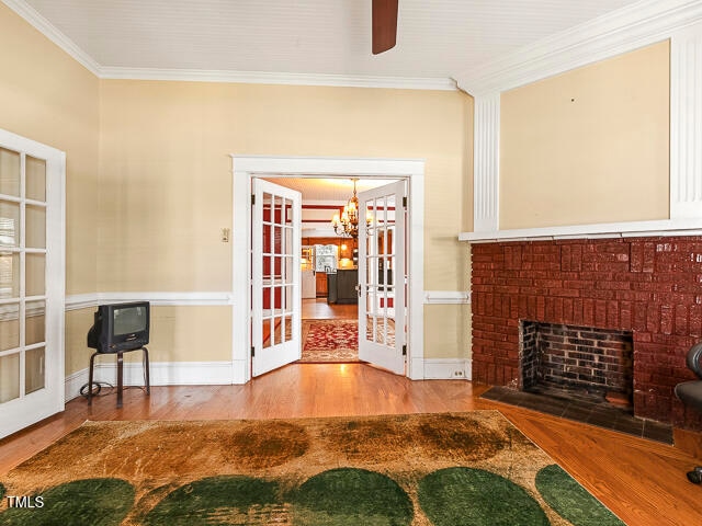 unfurnished living room with french doors, a notable chandelier, hardwood / wood-style flooring, and crown molding