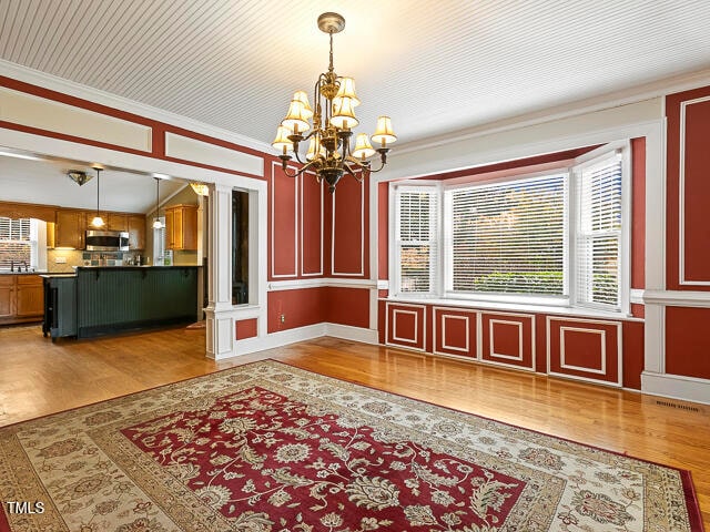 unfurnished dining area with a chandelier, hardwood / wood-style flooring, and ornamental molding