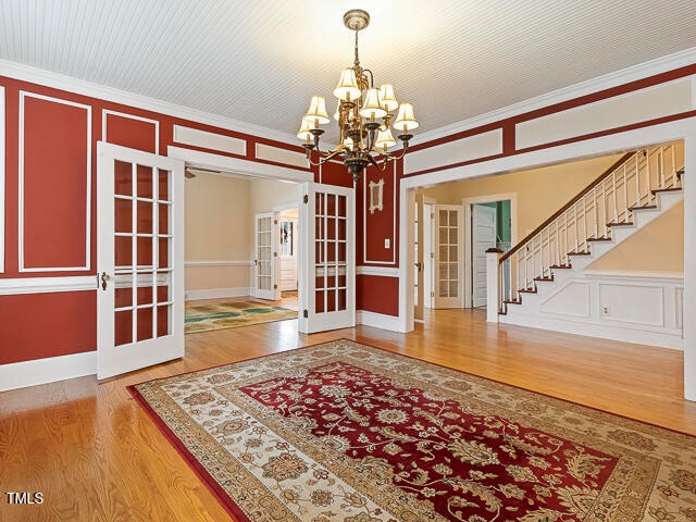 foyer featuring a chandelier, wood-type flooring, french doors, and crown molding