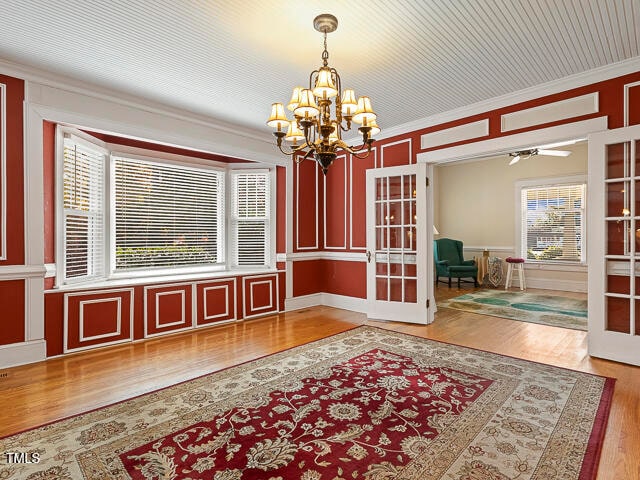 dining space featuring hardwood / wood-style floors, ceiling fan with notable chandelier, french doors, and crown molding