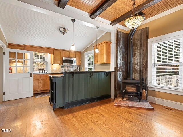 kitchen with lofted ceiling with beams, decorative light fixtures, a wood stove, wood ceiling, and light hardwood / wood-style flooring