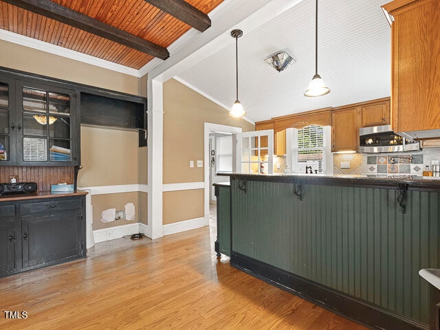 kitchen featuring light hardwood / wood-style floors, a breakfast bar area, backsplash, decorative light fixtures, and lofted ceiling with beams