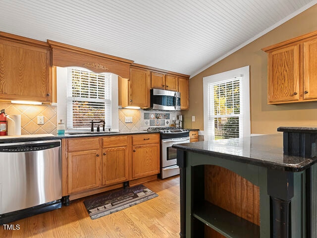 kitchen with light hardwood / wood-style floors, sink, appliances with stainless steel finishes, ornamental molding, and dark stone countertops