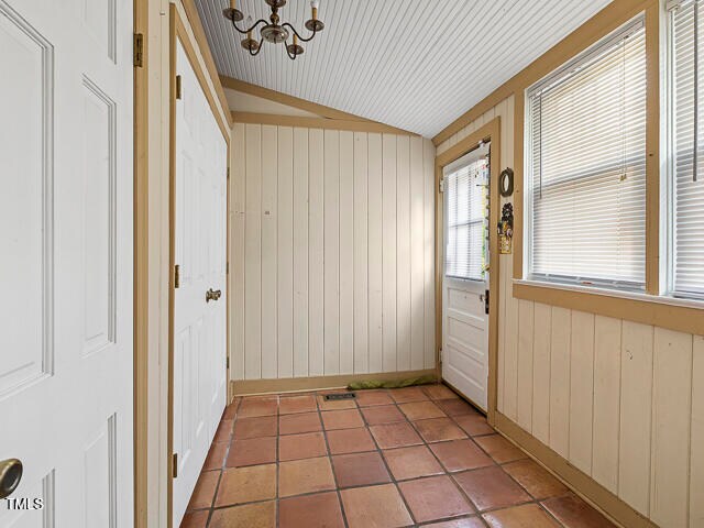 doorway to outside featuring wood ceiling, vaulted ceiling, an inviting chandelier, tile patterned flooring, and wood walls