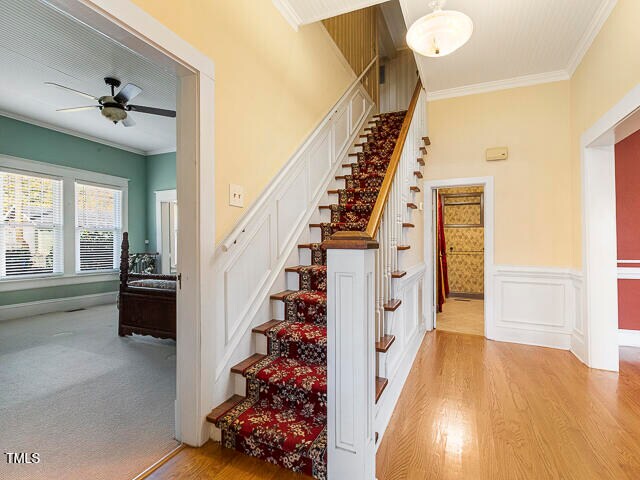 stairs featuring ceiling fan, wood-type flooring, and ornamental molding