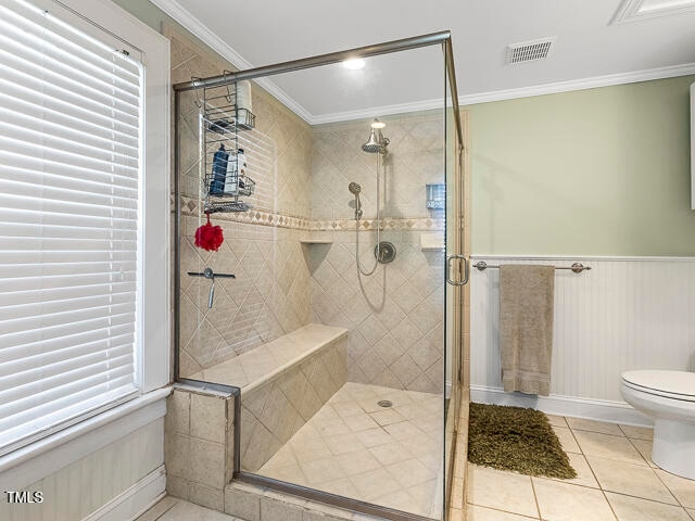 bathroom featuring toilet, tile patterned floors, crown molding, and a shower with shower door