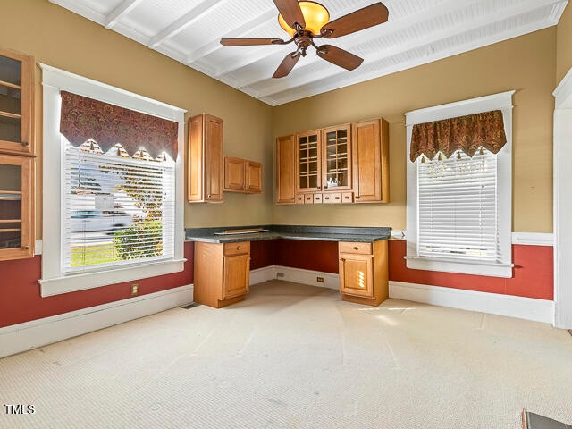 unfurnished office featuring built in desk, ceiling fan, and light colored carpet