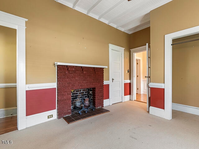 unfurnished living room with beamed ceiling, carpet flooring, and a brick fireplace