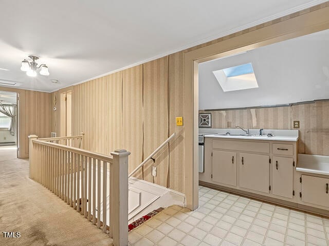 hall with light colored carpet, wooden walls, sink, crown molding, and a skylight