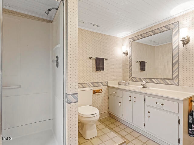 bathroom featuring vanity, crown molding, a shower with shower door, tile patterned floors, and toilet