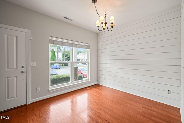 empty room featuring wooden walls, an inviting chandelier, and wood-type flooring