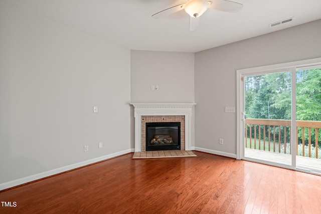 unfurnished living room with ceiling fan, hardwood / wood-style flooring, and a tiled fireplace