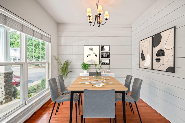 dining space with a notable chandelier, wood walls, and hardwood / wood-style floors