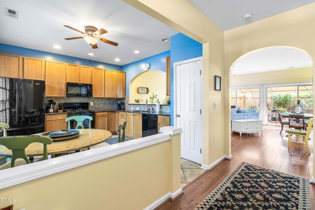 kitchen with light wood-type flooring, tasteful backsplash, black appliances, sink, and ceiling fan