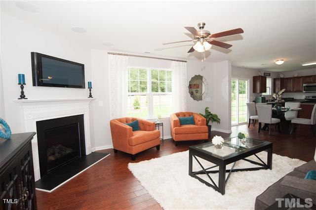 living room featuring dark wood finished floors, a ceiling fan, baseboards, and a fireplace with raised hearth