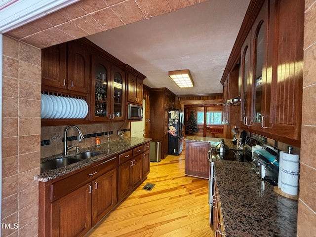 bar with sink, light hardwood / wood-style flooring, stainless steel appliances, backsplash, and dark stone countertops