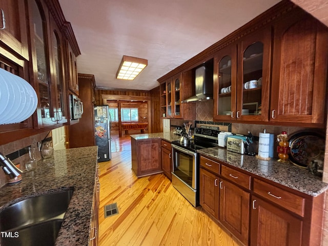 kitchen with dark stone countertops, wall chimney exhaust hood, stainless steel appliances, light wood-type flooring, and sink