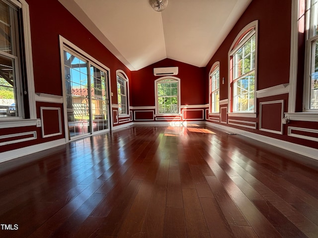 empty room with hardwood / wood-style flooring, lofted ceiling, plenty of natural light, and an AC wall unit