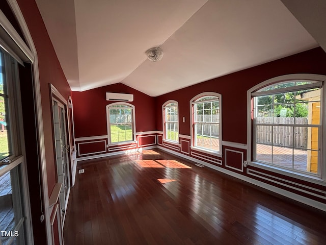 spare room featuring vaulted ceiling, a wall unit AC, and dark wood-type flooring