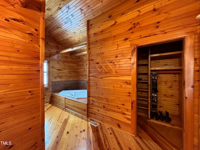 bathroom with lofted ceiling, wood-type flooring, a tub to relax in, and wooden walls