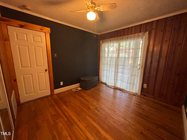 spare room featuring a textured ceiling, crown molding, ceiling fan, hardwood / wood-style flooring, and wooden walls