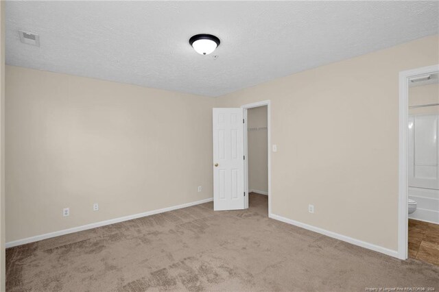 unfurnished bedroom with light carpet, a textured ceiling, and ensuite bathroom