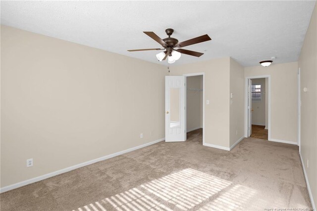 unfurnished bedroom featuring a textured ceiling, a walk in closet, a closet, light colored carpet, and ceiling fan