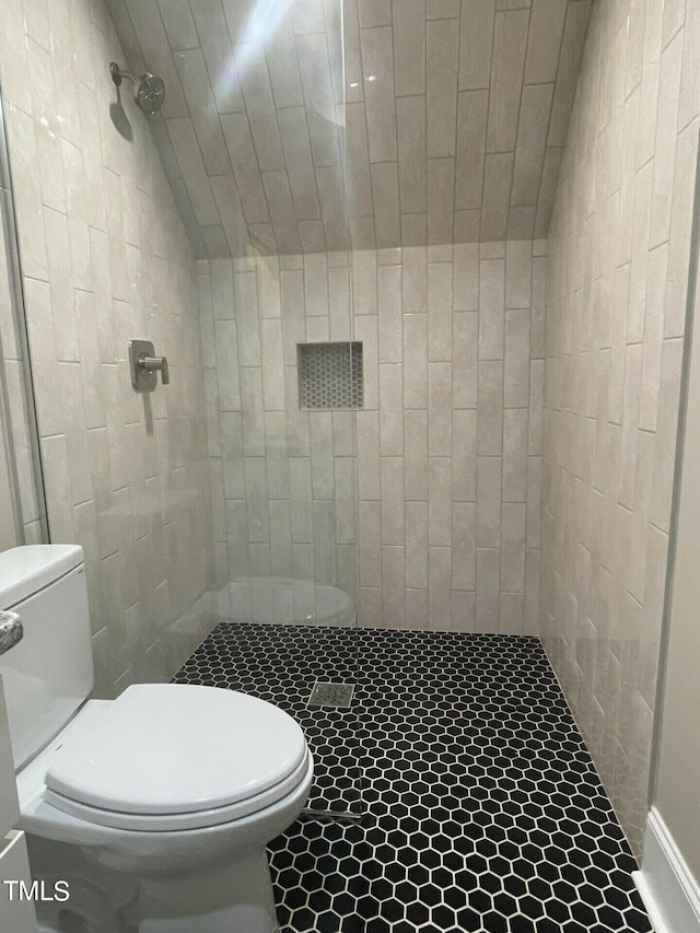 bathroom featuring tiled shower, toilet, and vaulted ceiling