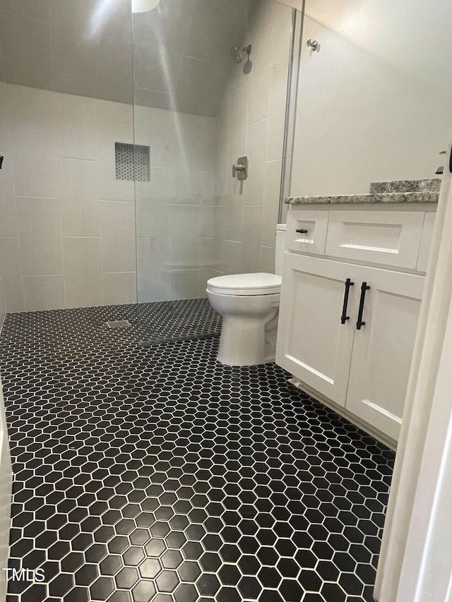 bathroom with toilet, tiled shower, and tile patterned flooring