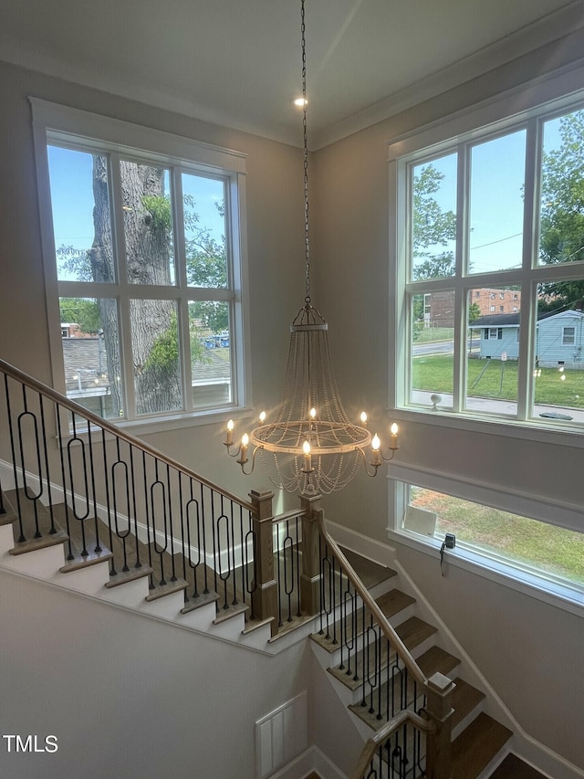 staircase with a wealth of natural light, a chandelier, and crown molding