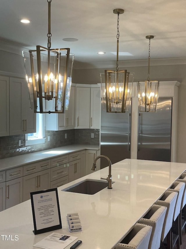 kitchen featuring pendant lighting, a notable chandelier, tasteful backsplash, sink, and stainless steel built in refrigerator